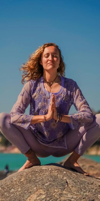 A woman practicing yoga on rocks in Rishikesh with a serene backdrop.
