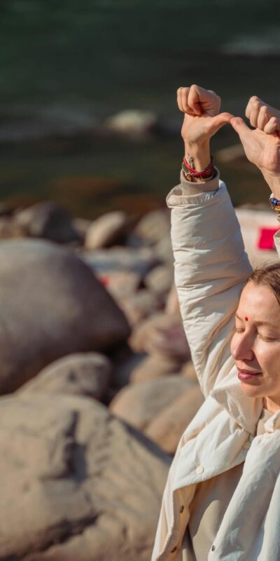 Relaxing by the Rishikesh river, a woman practices mindful meditation on rocky shores.