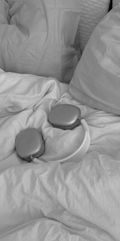 Stylish wireless headphones on a bed with pillows, in a monochrome theme.