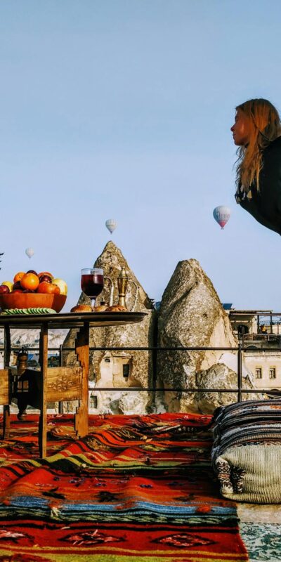 Woman performing yoga on a colorful Turkish rooftop, surrounded by hot air balloons in Cappadocia.